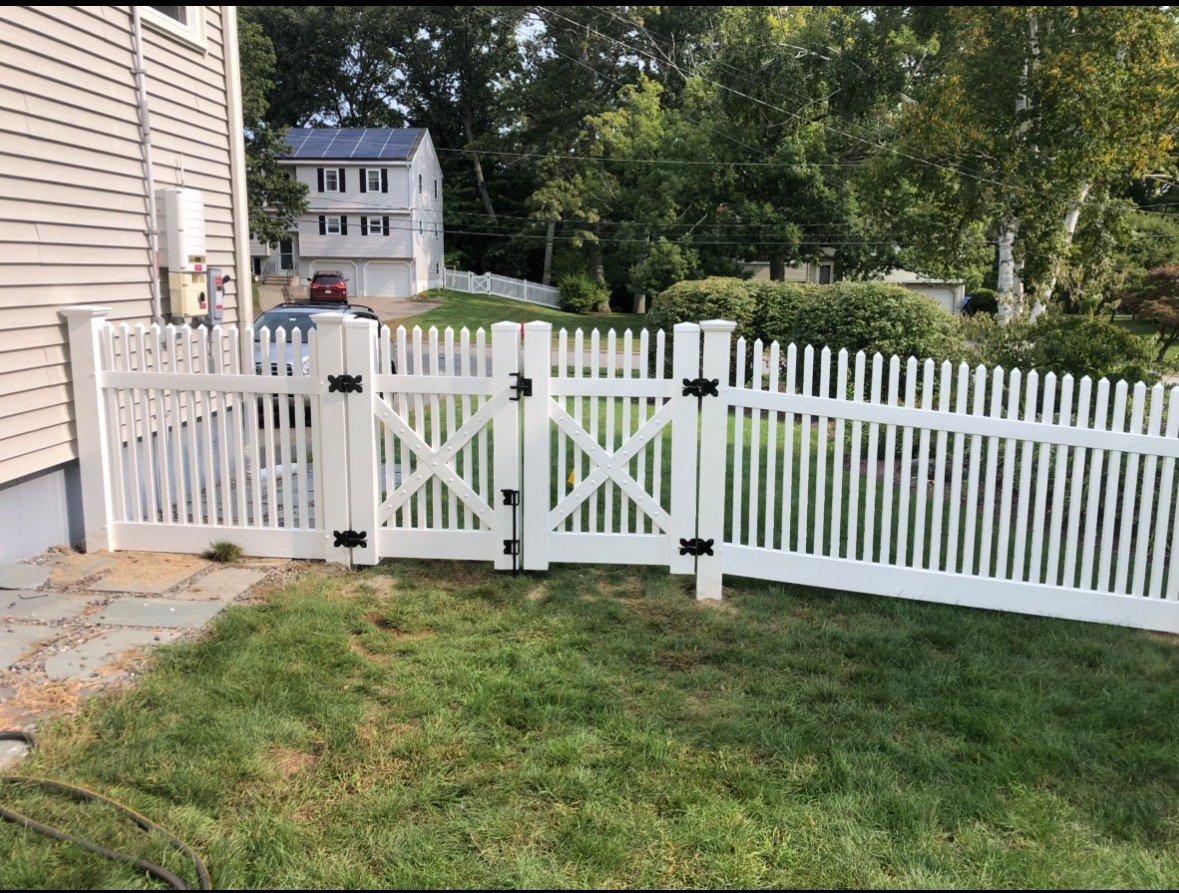 White picket fence with open gate in residential backyard, with house and trees in background