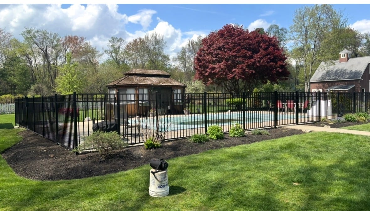 Fenced-in agricultural enclosure with metal gates in a pastoral landscape surrounded by trees and spring foliage
