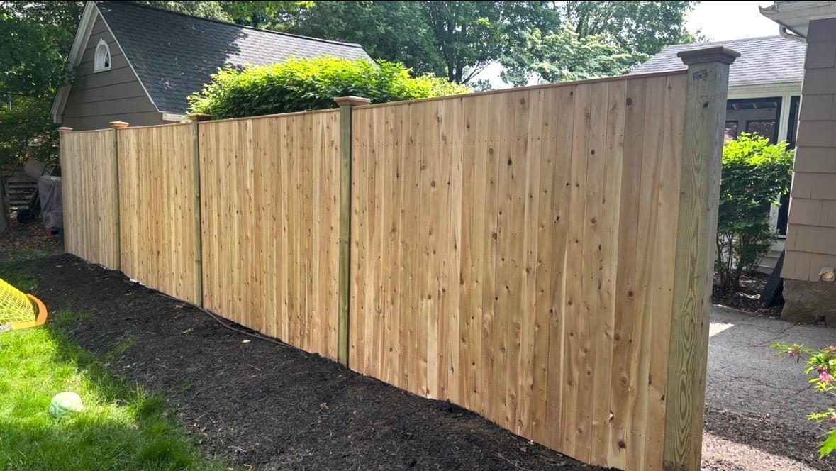 Newly installed wooden privacy fence bordering a residential property with green lawn and trees in background