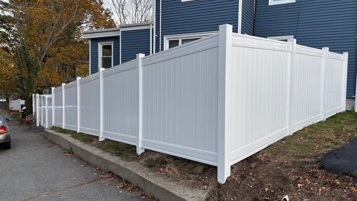 White vinyl privacy fence installed around a residential yard with blue house in background