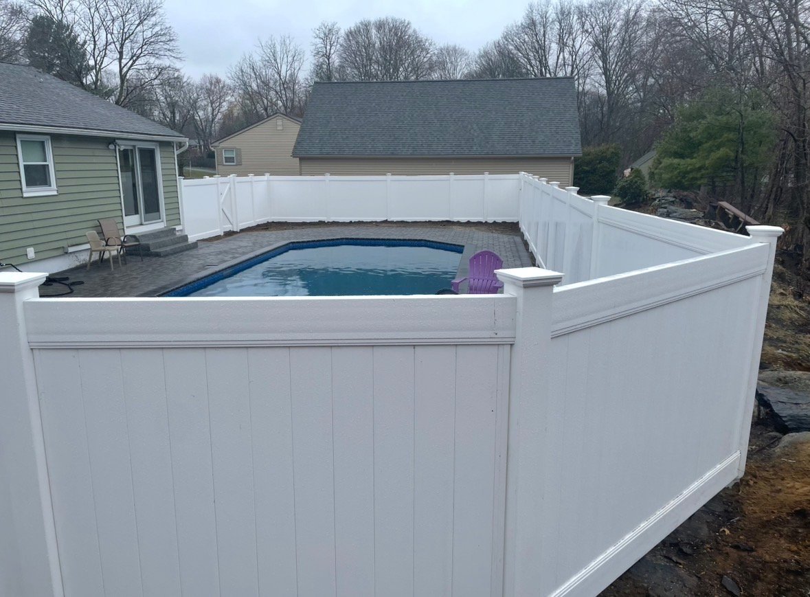 Above-ground swimming pool surrounded by white vinyl privacy fencing in a backyard with bare trees